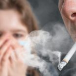 Passive Smoking. Man Is Smoking Cigarette And Woman Is Covering Her Face. A Lot Of Smoke Around.